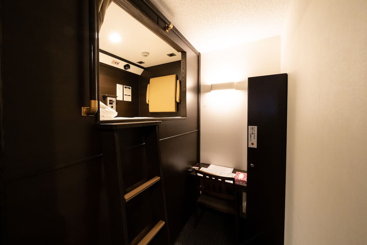 A narrow hallway with a dark wooden door, a small desk with a chair, and a mirror on the wall.
