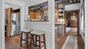 A kitchen with a stainless steel refrigerator, wooden stools, and a brick floor.