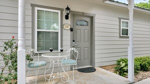 A house with a grey door, a window with blinds, and a porch with two chairs and two wine glasses.
