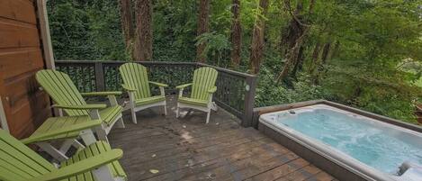 A wooden deck with three Adirondack chairs and a hot tub.