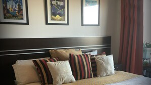 Un lit bien fait, avec une couvre-lit à motifs et plusieurs oreillers, une tête de lit sombre et des affiches encadrées accrochées au mur.