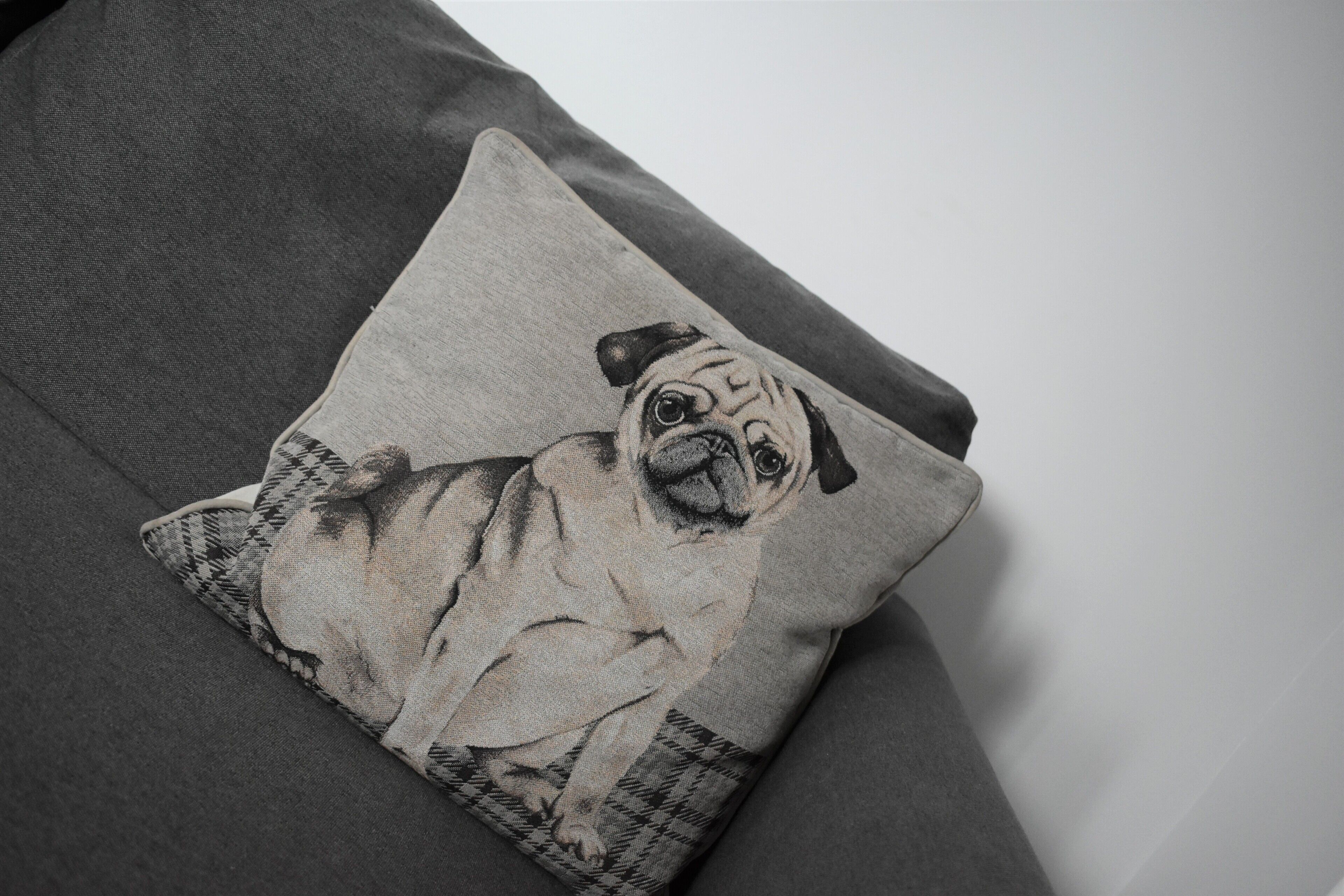A pillow with a pug dog design on a grey sofa.