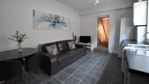 Ein modernes Wohnzimmer mit einem dunkelbraunen Ledersofa, einem kleinen runden Tisch mit einer Vase, einem Flachbildfernseher und einem großen abstrakten Gemälde an der Wand.