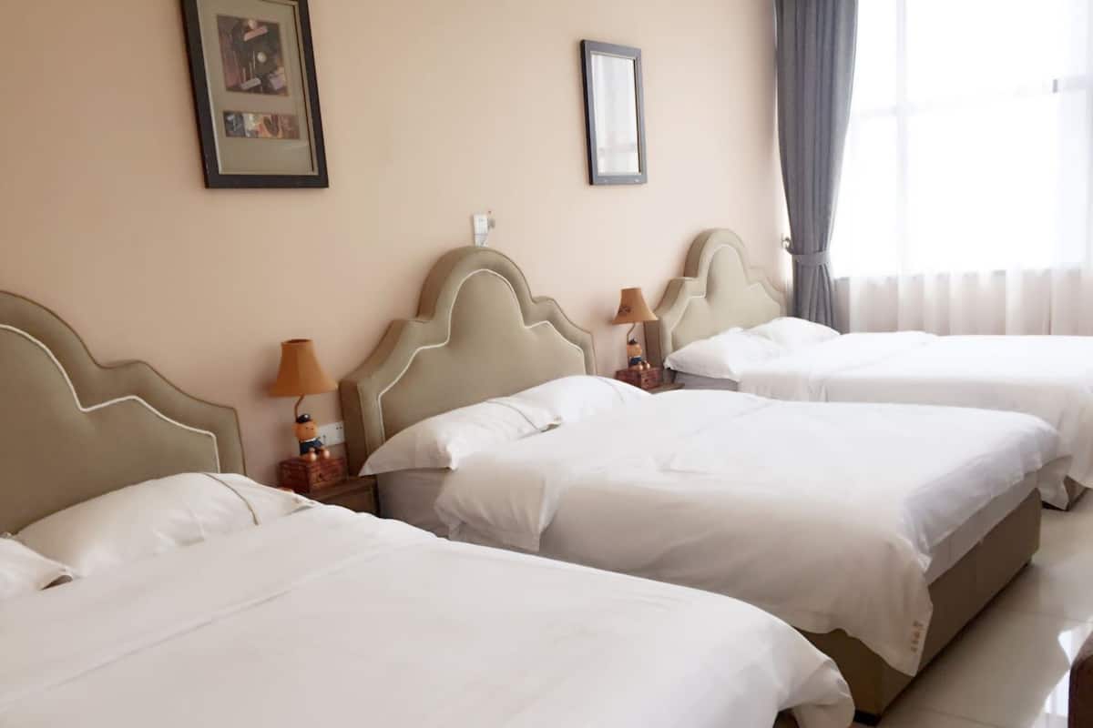 A hotel room with three single beds, each with a headboard and a nightstand with a lamp.