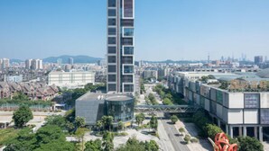 Un moderno edificio de gran altura con fachada de vidrio, rodeado de infraestructura urbana y vegetación.