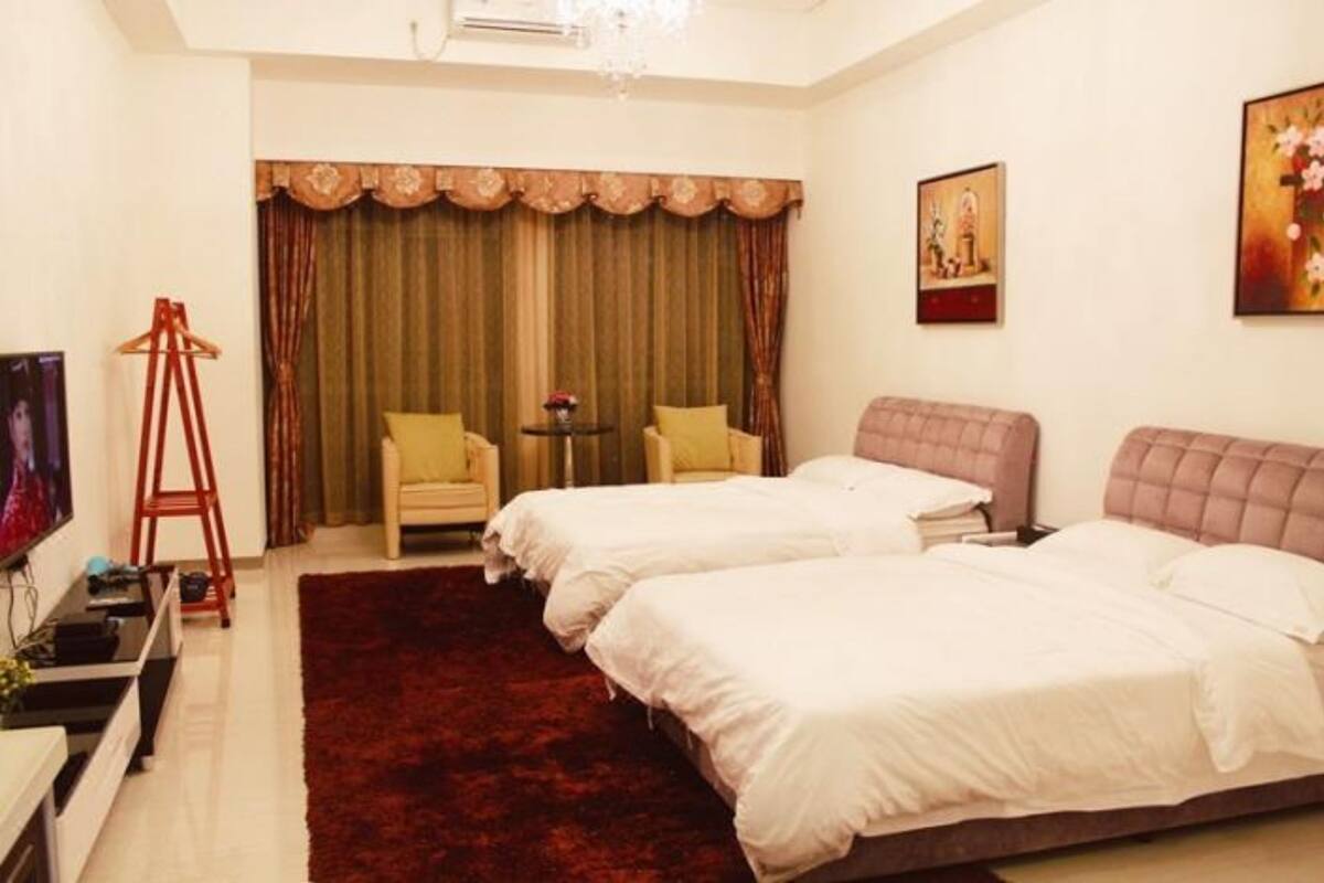A hotel room with two beds, a red carpet, a small table with a vase, and a painting on the wall.