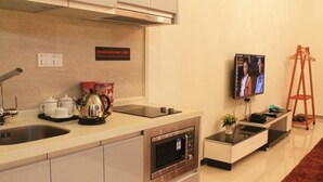 Una cocina moderna con horno empotrado, hervidor de agua y cafetera. Hay un televisor montado en la pared y una mesita con una planta.