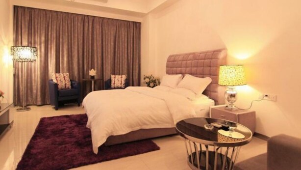 Una habitación de hotel moderna con una cama grande, una mesa redonda, una mesita de noche con lámpara y un candelabro.