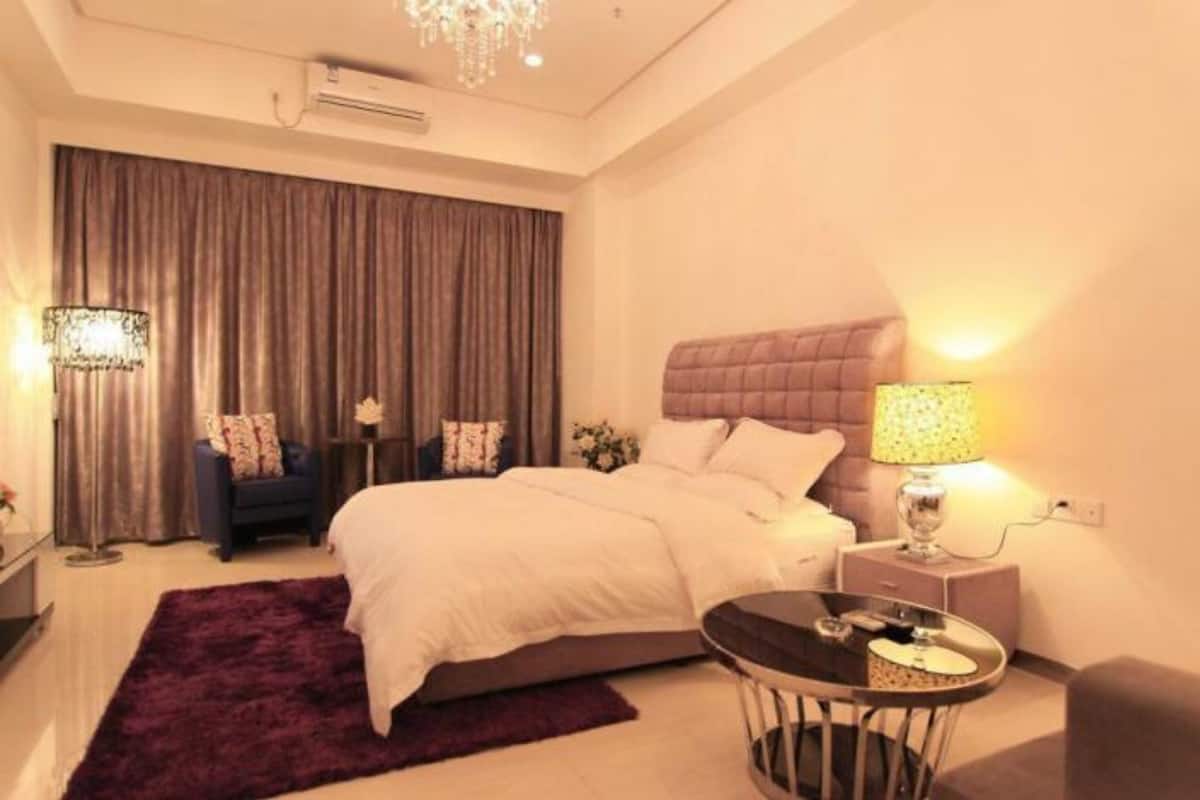 A modern hotel room with a large bed, a round table, a nightstand with a lamp, and a chandelier.