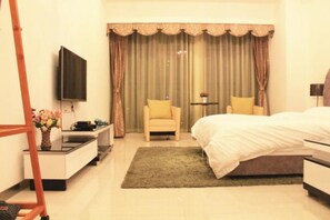 Habitación de hotel con cama, una silla, escritorio con televisor de pantalla plana y un amplio ventanal con cortinas.