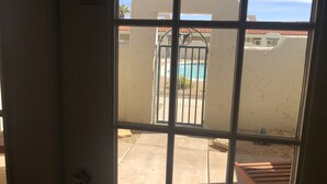 Blick durch ein Fenster mit einem Metallgitter, einem Pool und einem Gebäude mit weißer Fassade und roten Ziegeln.