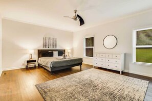 A bedroom with a bed, bedside tables, a dresser, a ceiling fan, and a window with blinds.