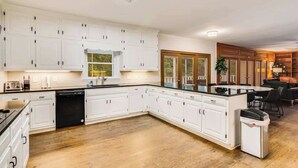 A modern kitchen with white cabinetry, a dishwasher, and a dining area with a black table and chairs. - Pool estate with soccer field, sleeps 16 (Lithonia)