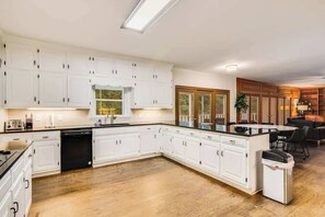 A modern kitchen with white cabinetry, a dishwasher, and a dining area with a black table and chairs.