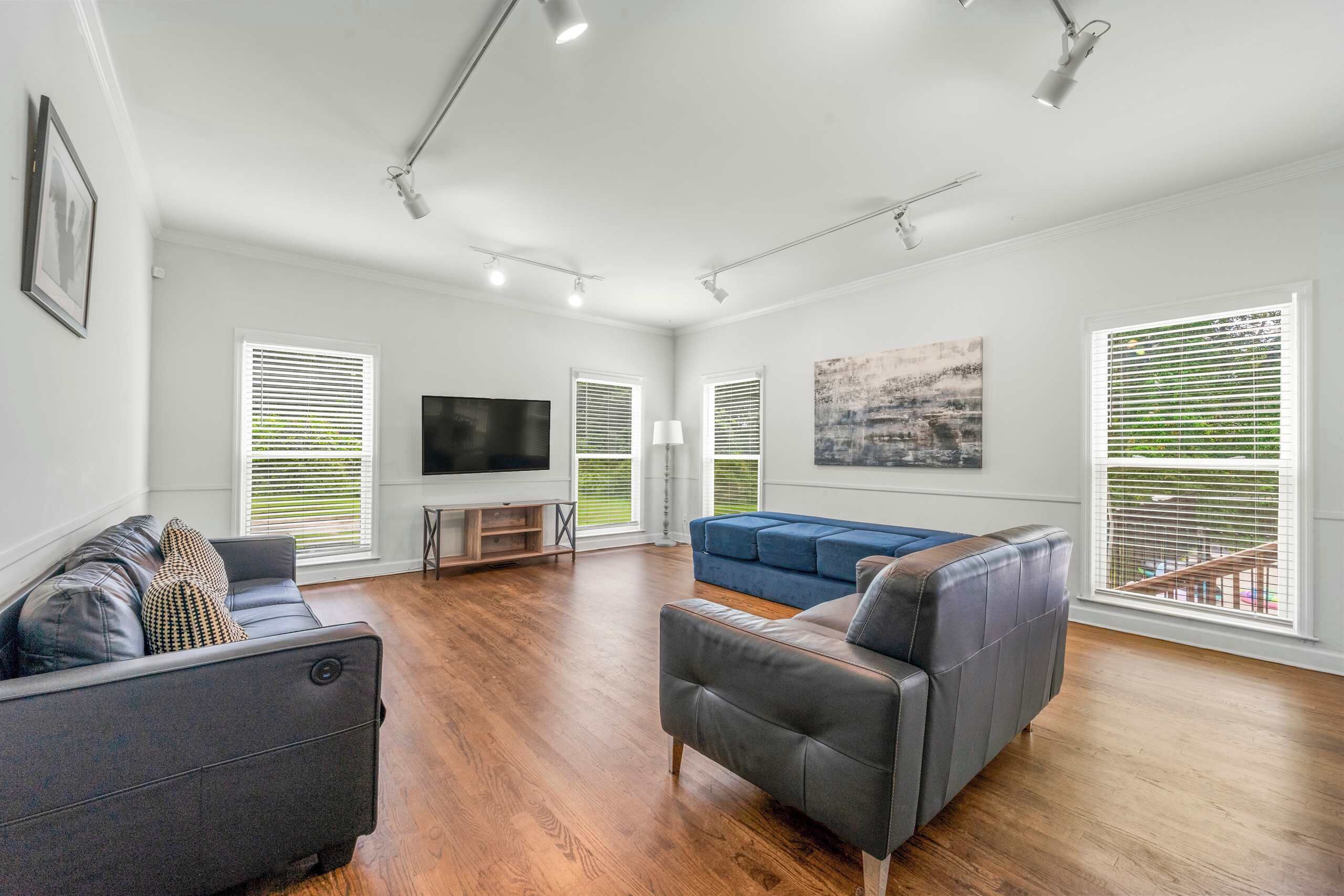 A spacious living room with hardwood flooring, a flat-screen TV, a blue sofa, and a grey armchair.