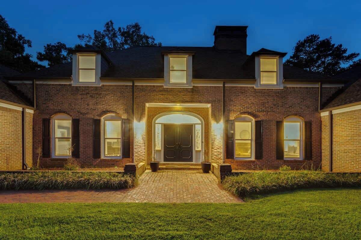 A two-story brick house with a central entrance, a covered porch, and a well-maintained lawn.