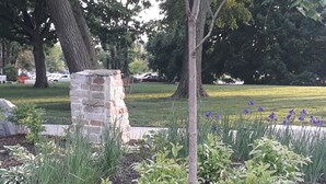 Un piló de pedra, un arbre i un llit de flors amb flors morades.