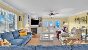 A living room with a blue sofa, a beige armchair, a glass coffee table, and a fireplace. - Tar Healin': Private Saltwater Pool and Ocean Views on Carolina Coast (Oak Island)