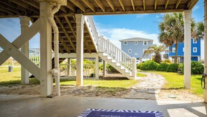 A covered outdoor area with a concrete floor, a wooden staircase, and a view of a residential building in the background. - Tar Healin': Private Saltwater Pool and Ocean Views on Carolina Coast (Oak Island)