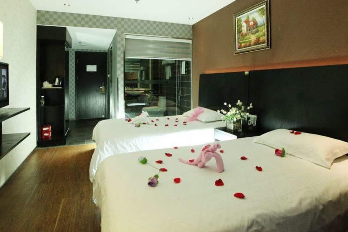 A hotel room with two beds, a painting on the wall, and a desk with a vase of flowers.