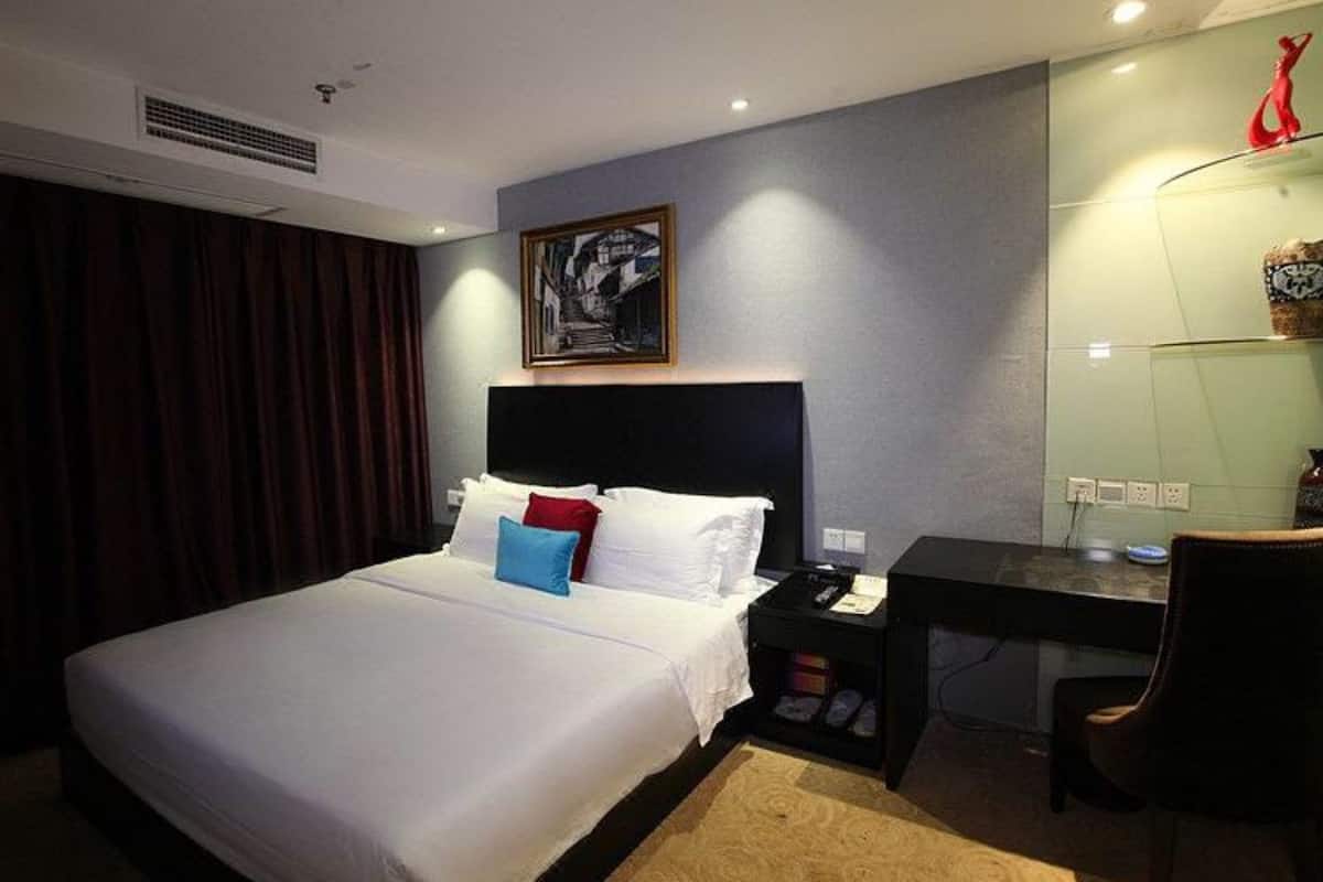 A hotel room with a large bed, a desk, a chair, and a painting on the wall.