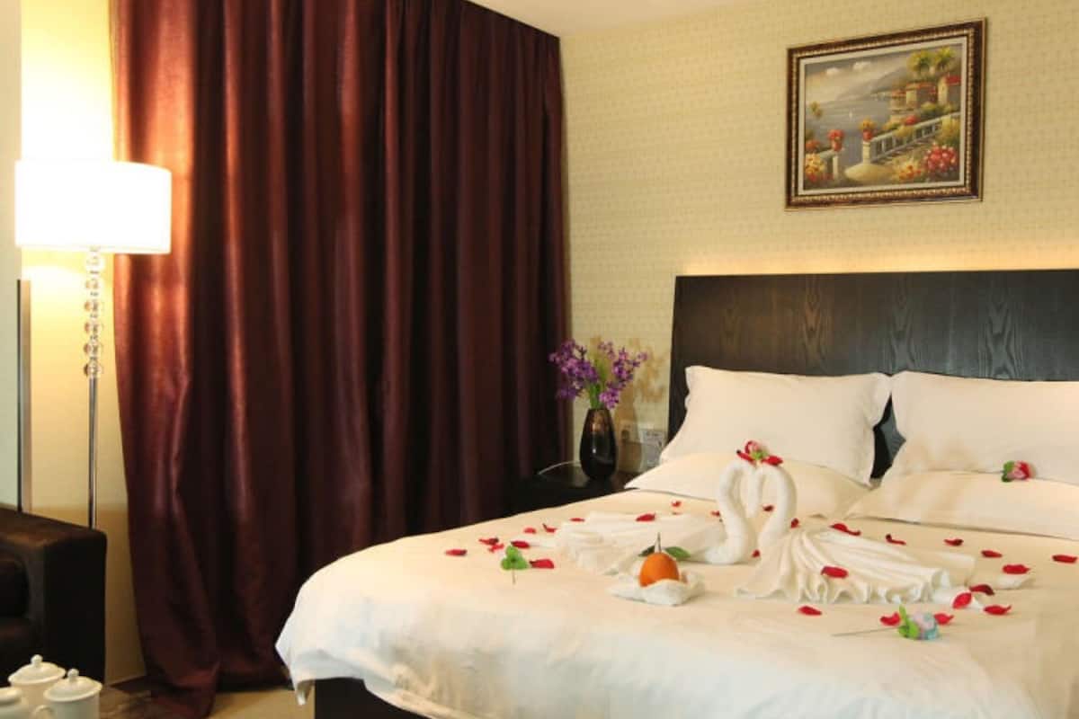 A hotel room with a large bed, a nightstand, a lamp, and a painting on the wall.