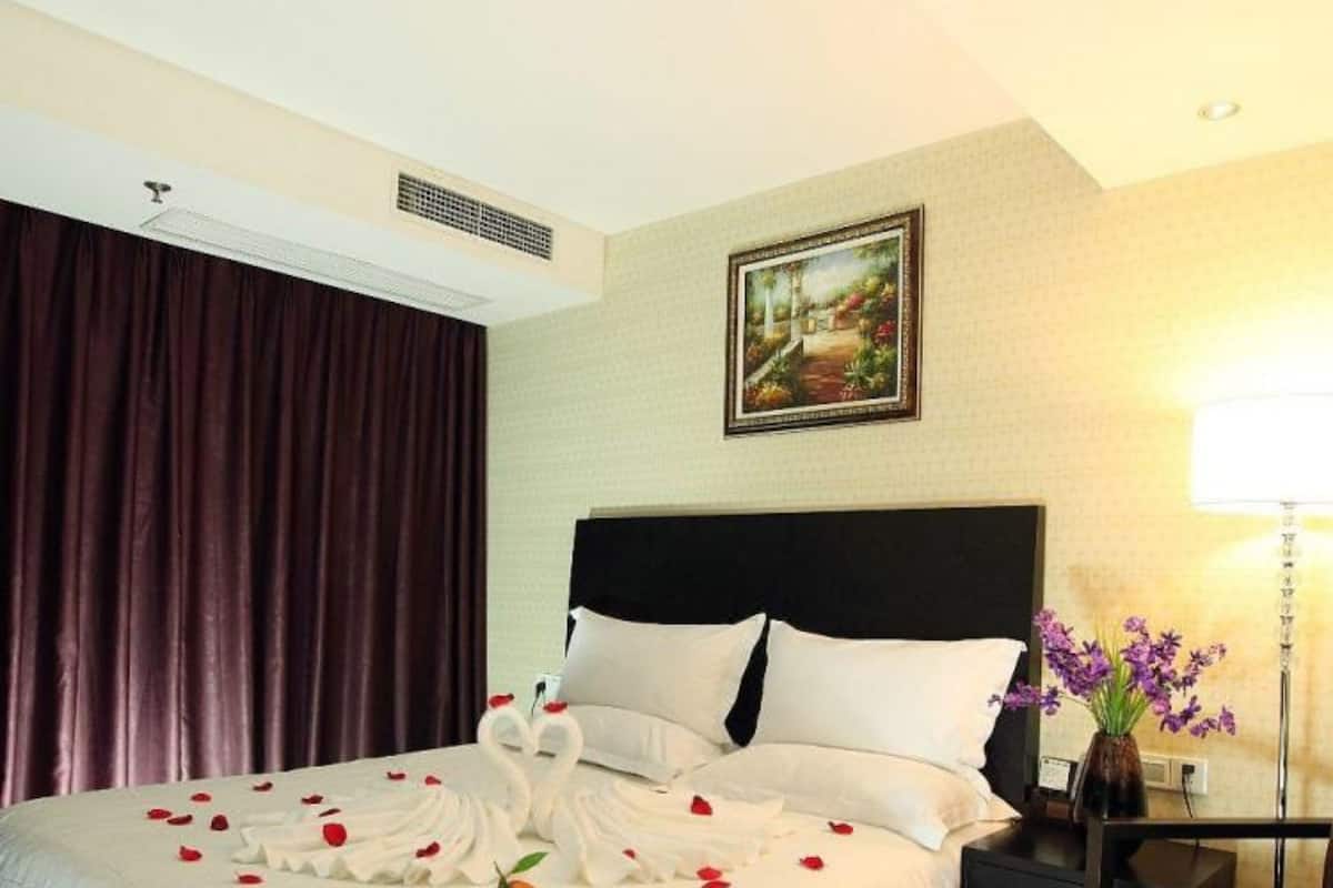 A hotel room with a large bed, a nightstand, a desk, a chair, a lamp, and a painting on the wall.