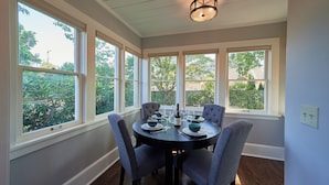 A dining area with a round table set for four, surrounded by large windows offering a view of greenery and buildings.