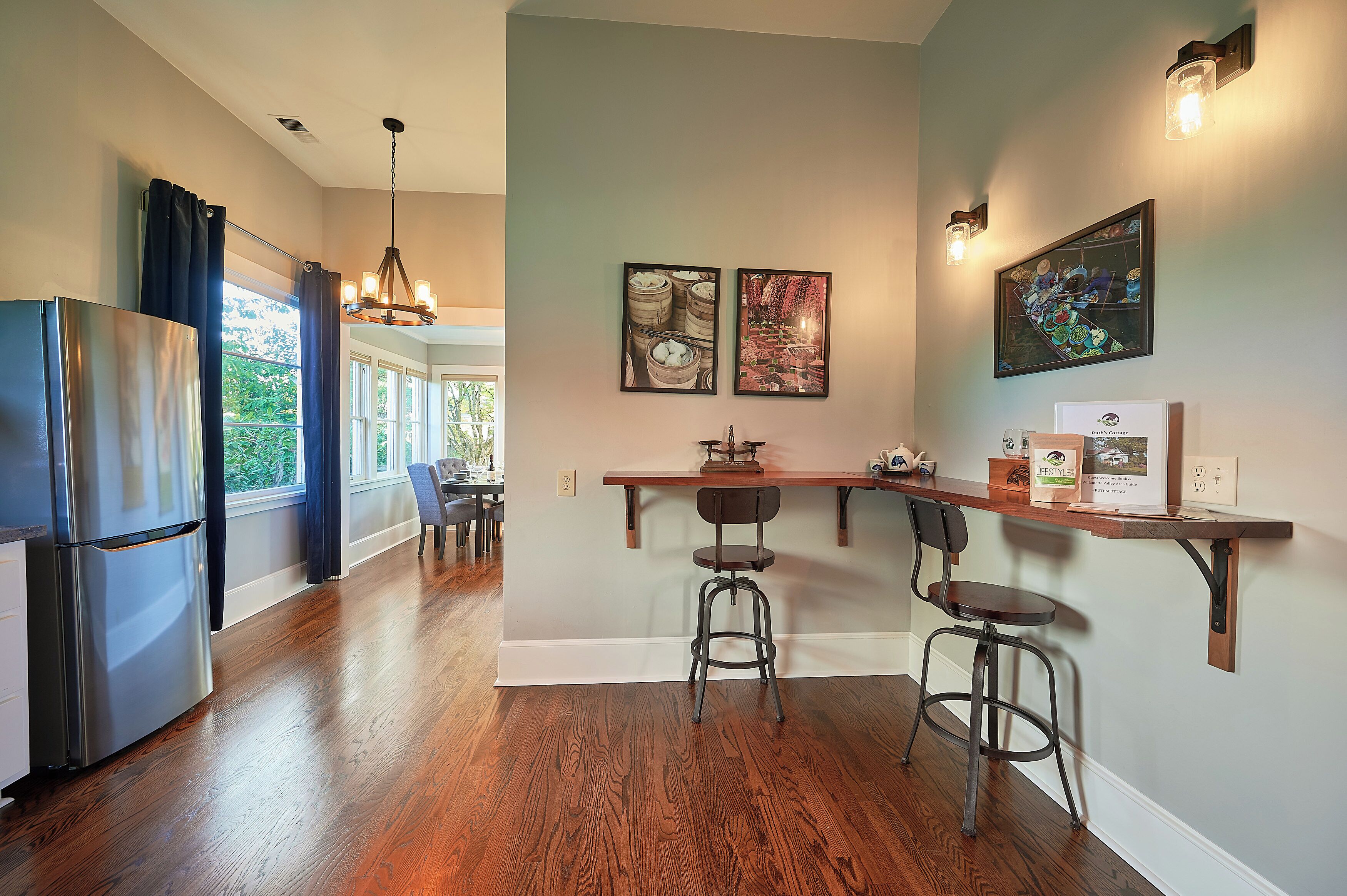 A kitchen with a refrigerator, wooden bar counter, stools, and artwork on the wall.
