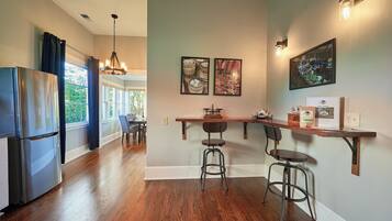 A kitchen with a refrigerator, wooden bar counter, stools, and artwork on the wall.