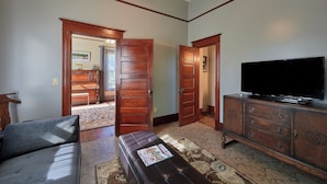 A living room with a sofa, a coffee table, a television on a wooden cabinet, and a door leading to another room.