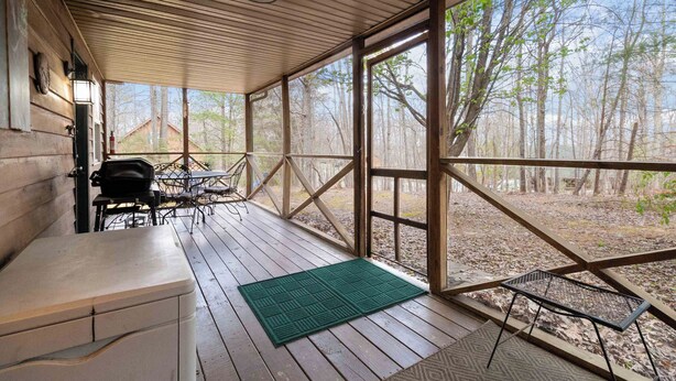 A covered porch with a grill, outdoor seating, and a view of the forest.