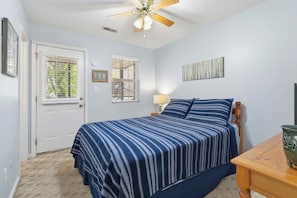 A bedroom with a bed, a ceiling fan, a door, and a window.
