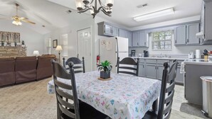 A dining area with a table set for four, a chandelier, and a kitchen in the background.