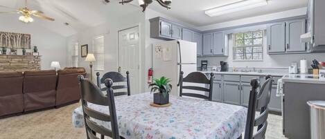 A dining area with a table set for four, a chandelier, and a kitchen in the background.