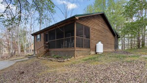 A wooden cabin with a porch, large windows, and a water tank.