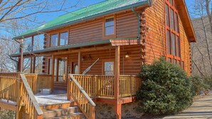 A log cabin with a porch, a stone foundation, and a green roof. - MAJESTIC MEMORIES - 3 LEVEL CUSTOM CABIN! (Sevierville)