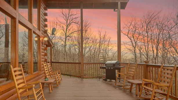 A wooden deck with rocking chairs and a barbecue grill, overlooking a forested area during sunset. - MAJESTIC MEMORIES - 3 LEVEL CUSTOM CABIN! (Sevierville)