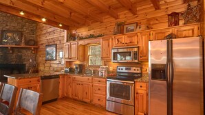 A log cabin-style kitchen with wooden cabinets, a stone fireplace, a stainless steel refrigerator, and a built-in oven. - MAJESTIC MEMORIES - 3 LEVEL CUSTOM CABIN! (Sevierville)