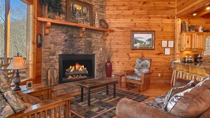 A cozy cabin interior with a stone fireplace, wooden furniture, and a view of the outdoors. - MAJESTIC MEMORIES - 3 LEVEL CUSTOM CABIN! (Sevierville)