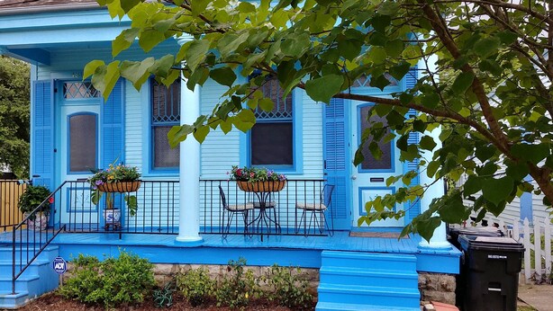A blue house with a porch, two flower baskets, and a trash can.