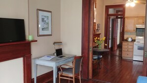 A room with a desk, chair, TV, and a small table with flowers.
