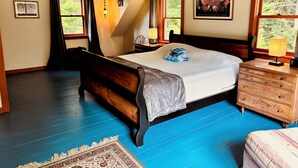 A bedroom with a large bed, a wooden dresser, a nightstand, a lamp, and a window with curtains.