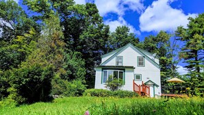 A white house with a green roof, surrounded by lush greenery and trees.