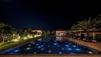 Una piscina con superficie de azulejos, rodeada de palmeras y sillas de descanso.