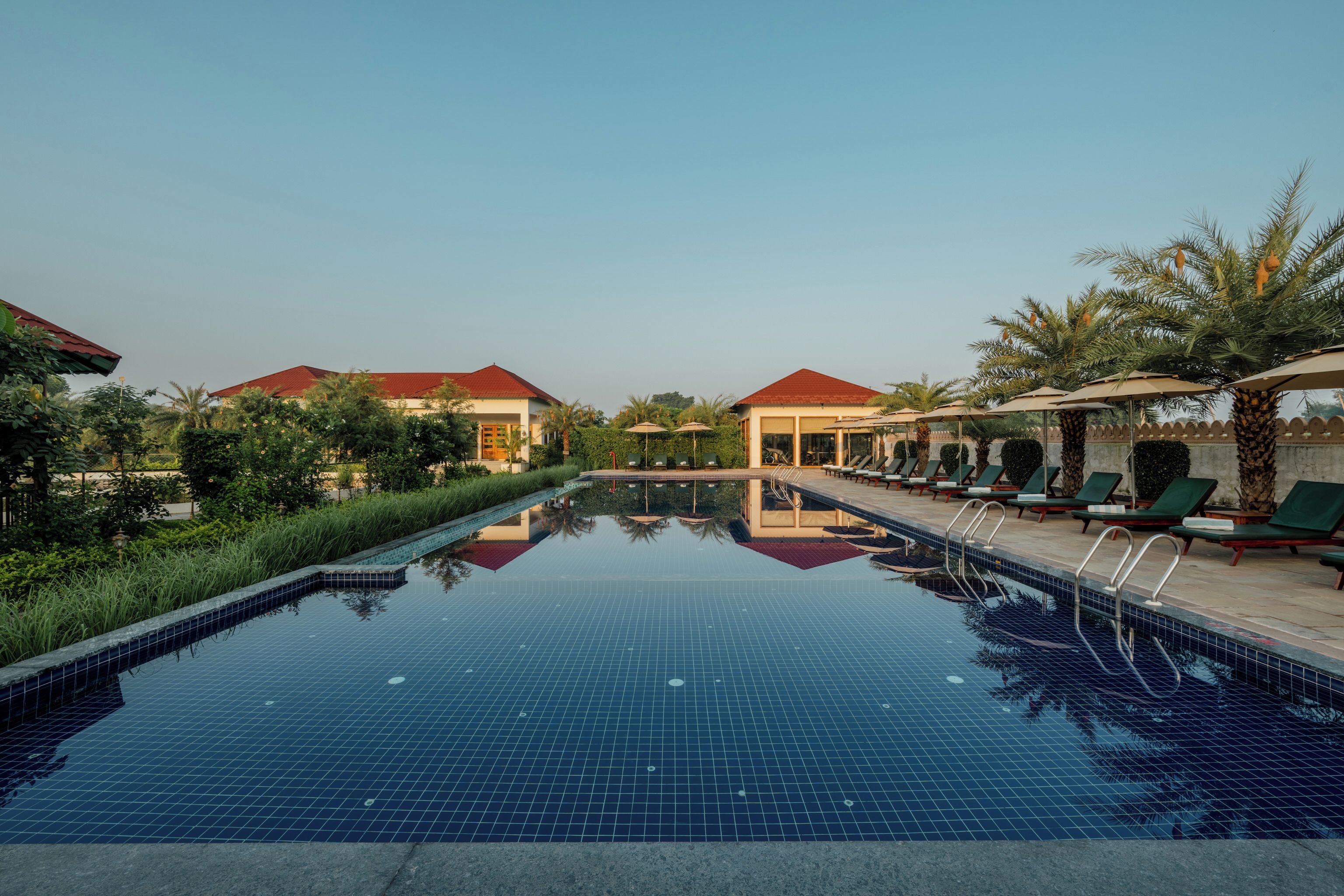 A swimming pool with lounge chairs and umbrellas, surrounded by greenery and buildings with red roofs.