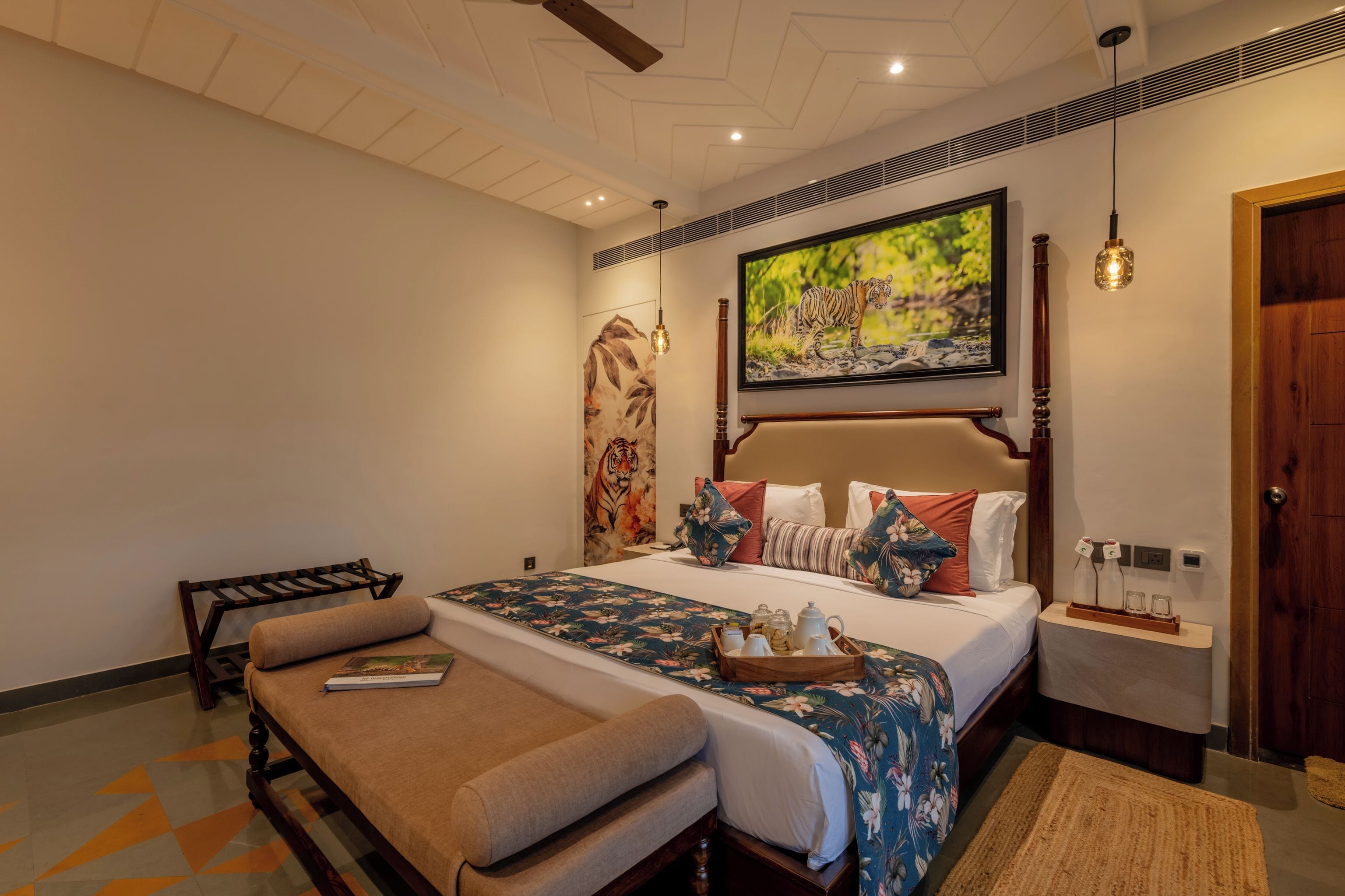 A hotel room with a large bed, a bench, a wooden headboard, a painting, and a nightstand with a lamp.