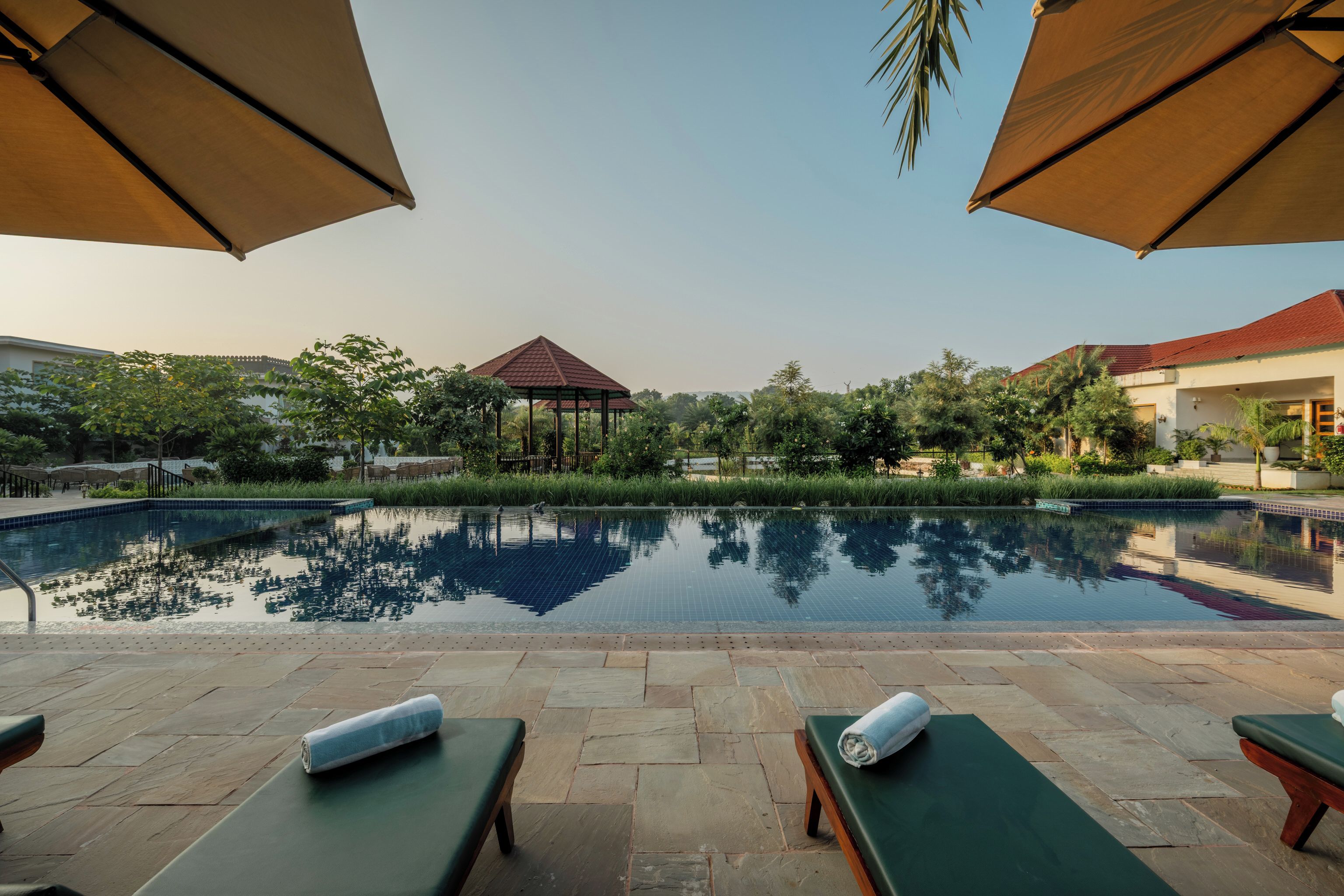 A swimming pool with lounge chairs and umbrellas, surrounded by greenery and a gazebo.