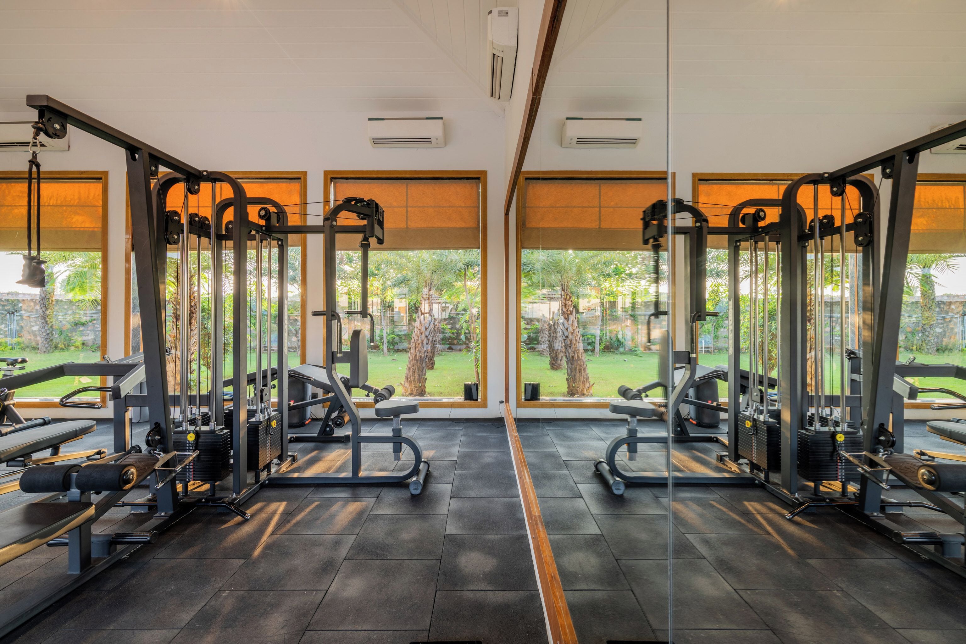 A gym with mirrored walls, exercise equipment, and large windows overlooking a garden.
