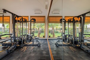 Un gimnasio con paredes espejadas, equipo de ejercicio y grandes ventanales con vistas a un jardín.